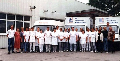 Gruppenfoto von Menschen in Arbeitskleidung vor zwei Lieferfahrzeugen mit dem Schriftzug „Ostendorfer Mühlenbäcker“.